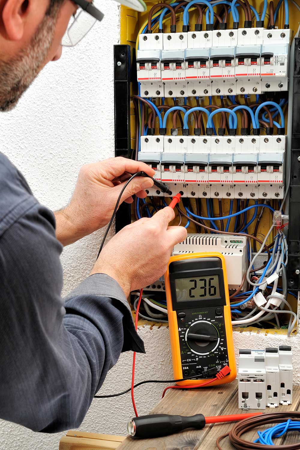 Worker uses a digital multimeter to test wires inside an open electrical service panel.