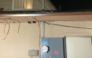 Close-up of exterior electrical setup: conduit, meter, and scattered wires.