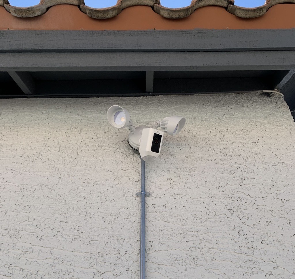 Image-2025-05-27T113232.369 Outdoor wall with a white motion sensor and a two-bulb lantern-style light fixture; conduit runs up the wall.