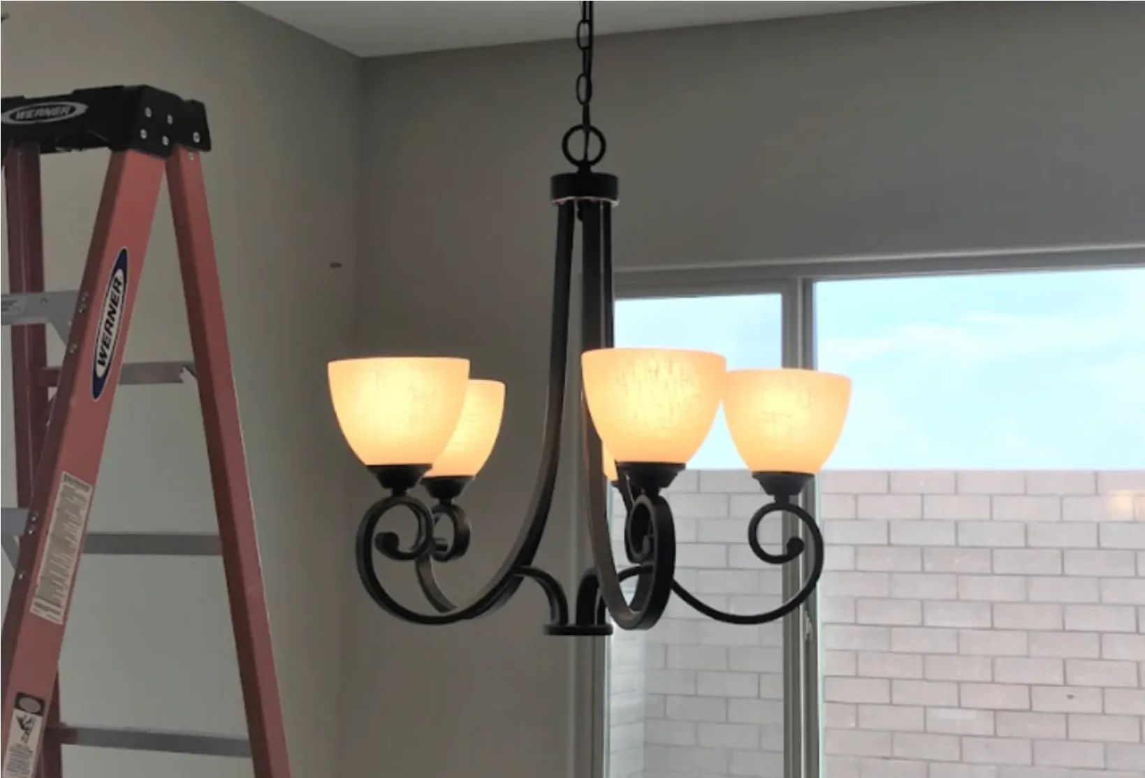 Indoor chandelier with several frosted-glass shades hanging from ceiling; red ladder rests nearby.
